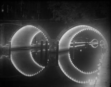 821049 Gezicht op de verlichte Hamburgerbrug over de Oudegracht te Utrecht, bij avond.